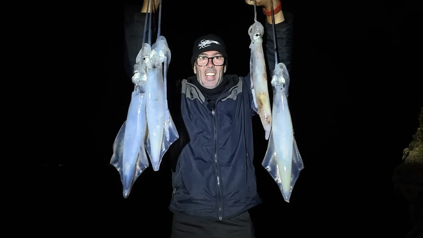 Pescador mostrando una captura doble de calamares de noche